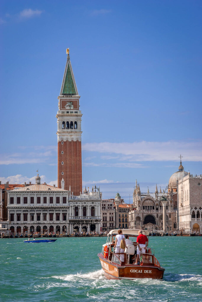 Auf diesem Farbfoto blickt man über das blaugrüne Meer auf Venedig. Auf dem Wasser befinden sich noch zwei weitere Boote.