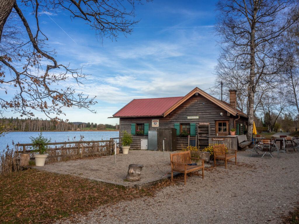 Der kleine Biergarten vor dem idyllisch am Bayersoiener Seeufer gelegenen Kiosks Fischerhäusl umrahmt von Bäumen.
